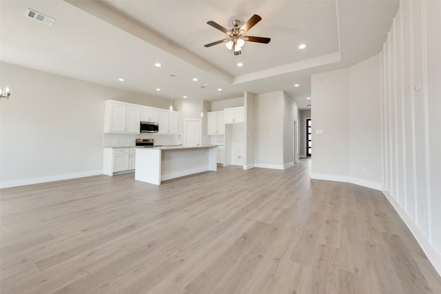 unfurnished living room featuring a tray ceiling, light wood-type flooring, and ceiling fan with notable chandelier