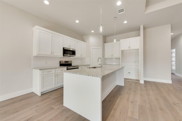 kitchen featuring white cabinetry, a center island with sink, stainless steel appliances, decorative light fixtures, and light stone countertops