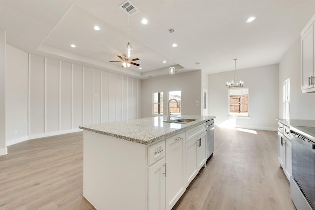 kitchen featuring sink, light stone counters, dishwasher, white cabinets, and a kitchen island with sink