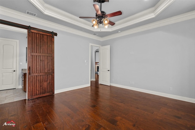 unfurnished room with ornamental molding, wood-type flooring, ceiling fan, a raised ceiling, and a barn door