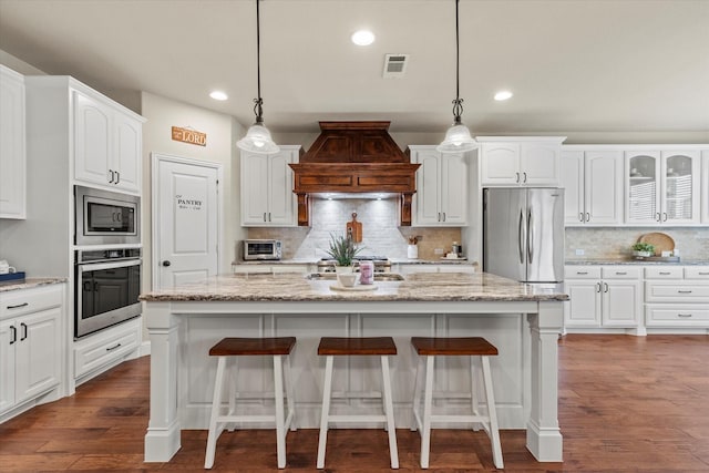 kitchen featuring premium range hood, pendant lighting, a center island, stainless steel appliances, and white cabinets