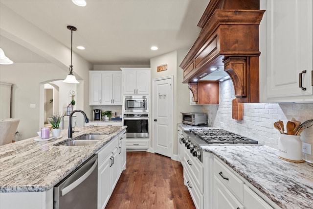 kitchen with stainless steel appliances, white cabinets, pendant lighting, sink, and a kitchen island with sink