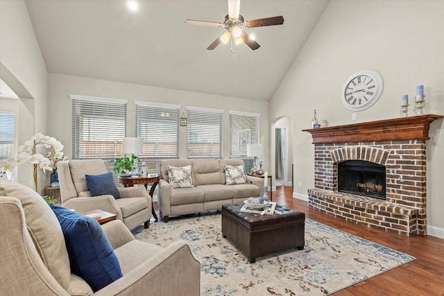 living room with light wood-type flooring, ceiling fan, high vaulted ceiling, and a fireplace