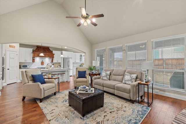 living room with ceiling fan, high vaulted ceiling, wood-type flooring, and sink