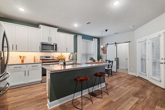 kitchen with a barn door, decorative light fixtures, stainless steel appliances, and white cabinets