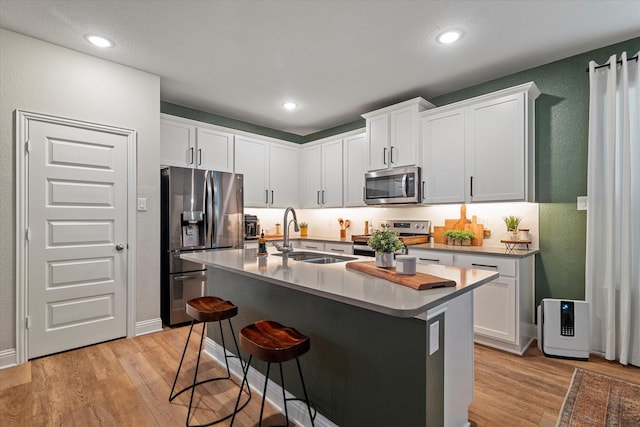 10012 Travis Dr, Providence Village, TX 76227 - kitchen with stainless steel appliances, a sink, a textured wall, light wood-style flooring, and a kitchen bar