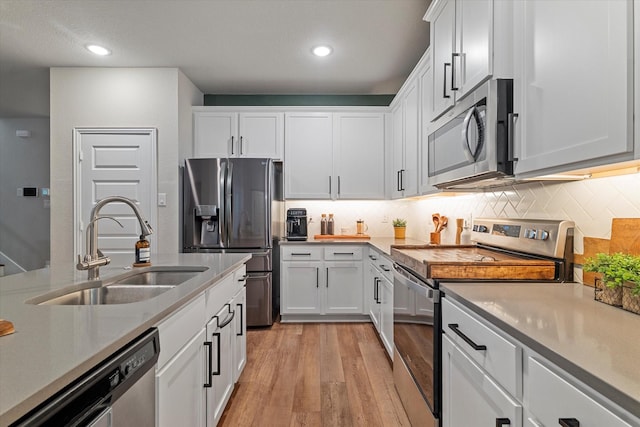 kitchen with light wood-type flooring, sink, tasteful backsplash, appliances with stainless steel finishes, and white cabinets