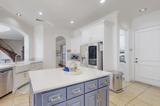 kitchen with light tile patterned floors, sink, appliances with stainless steel finishes, a center island, and white cabinetry