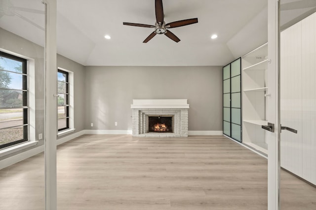 unfurnished living room with a brick fireplace, light wood-type flooring, lofted ceiling, and ceiling fan