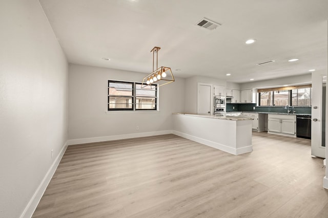 kitchen featuring appliances with stainless steel finishes, light wood-type flooring, white cabinetry, pendant lighting, and kitchen peninsula