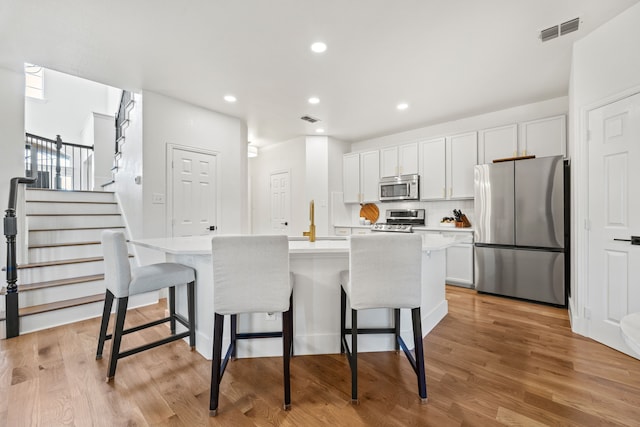 kitchen with a center island with sink, a kitchen bar, appliances with stainless steel finishes, and white cabinetry