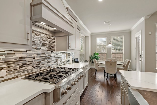 kitchen with stainless steel gas cooktop, custom range hood, light countertops, hanging light fixtures, and crown molding