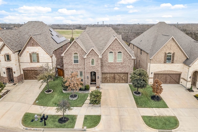 french country style house featuring a garage, concrete driveway, brick siding, and roof with shingles