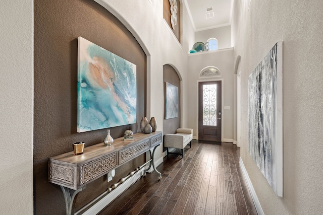 foyer entrance featuring dark wood-type flooring, a high ceiling, visible vents, baseboards, and ornamental molding