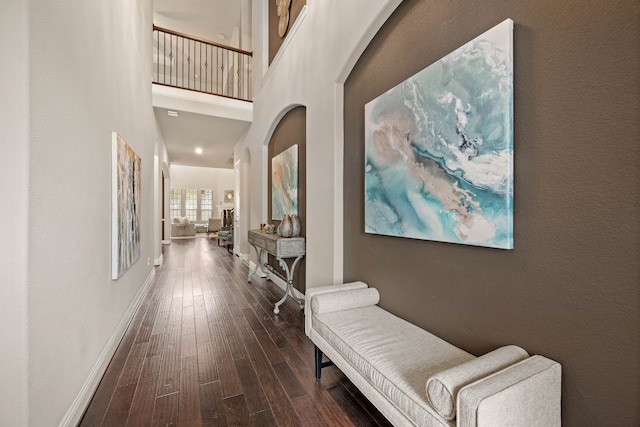 corridor featuring arched walkways, dark wood-style flooring, a towering ceiling, and baseboards