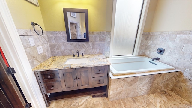 bathroom with tile walls, vanity, and tiled tub