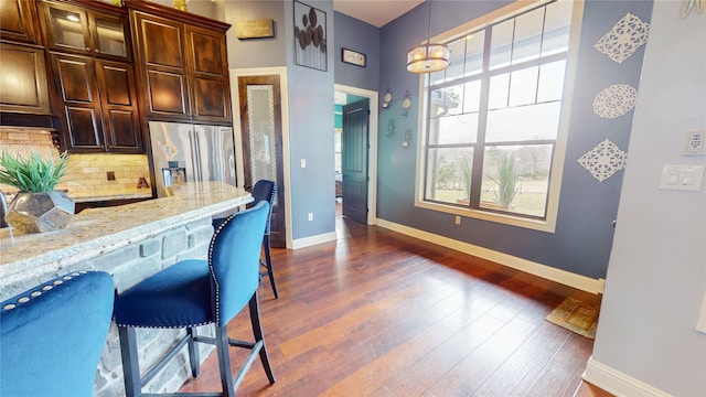 kitchen featuring tasteful backsplash, a kitchen breakfast bar, pendant lighting, dark hardwood / wood-style flooring, and stainless steel fridge with ice dispenser