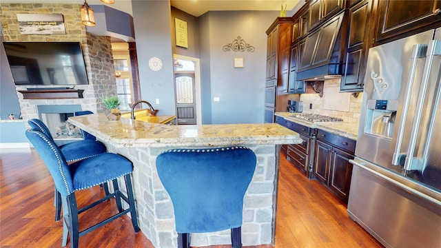 kitchen with stainless steel appliances, custom range hood, light stone counters, and a kitchen island with sink