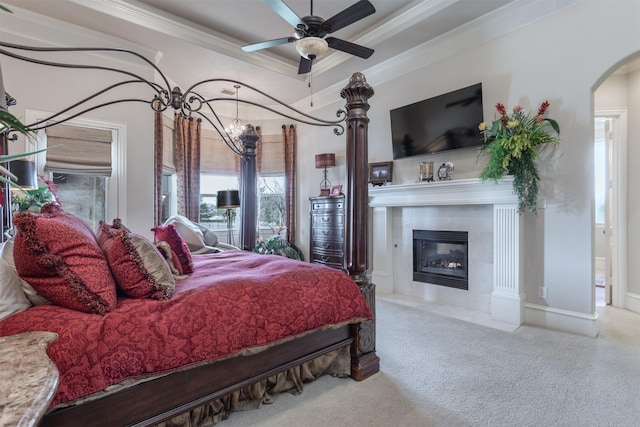 bedroom with arched walkways, a tray ceiling, light colored carpet, ornamental molding, and a tile fireplace