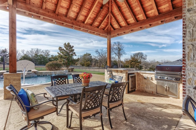 view of patio featuring an outdoor kitchen, a grill, fence, a fenced in pool, and outdoor dining space