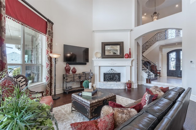 living area with arched walkways, a fireplace with raised hearth, a towering ceiling, stairway, and wood finished floors