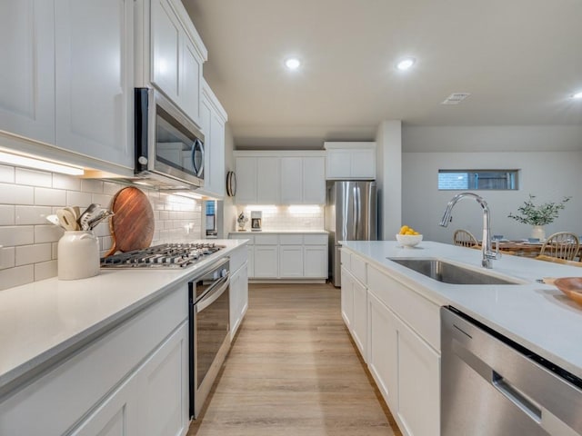 kitchen with sink, backsplash, white cabinetry, light hardwood / wood-style floors, and stainless steel appliances