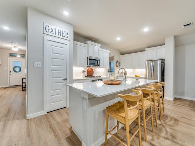 kitchen with sink, a center island with sink, white cabinets, and a breakfast bar area