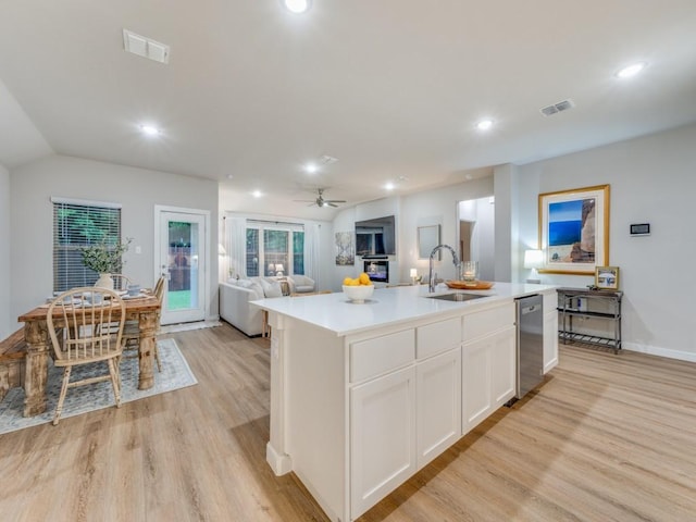 kitchen featuring sink, light wood-type flooring, dishwasher, white cabinets, and an island with sink