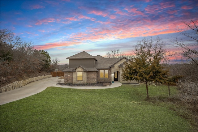 view of front of property featuring driveway, brick siding, a front lawn, and roof with shingles