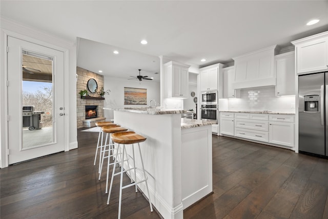 kitchen featuring light stone counters, dark wood-style flooring, tasteful backsplash, appliances with stainless steel finishes, and white cabinetry