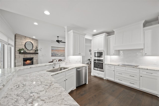 kitchen featuring appliances with stainless steel finishes, dark wood-type flooring, light stone countertops, white cabinetry, and a sink