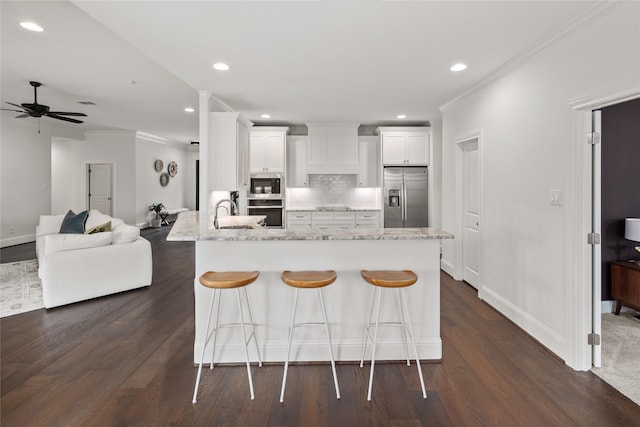 kitchen featuring stainless steel appliances, white cabinetry, open floor plan, light stone countertops, and tasteful backsplash