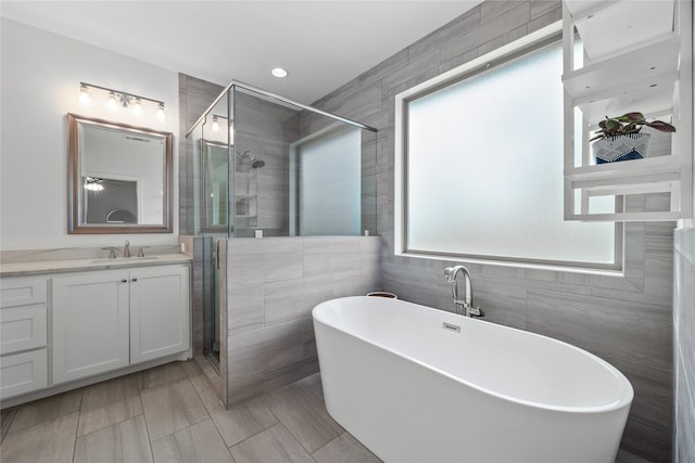 bathroom featuring a stall shower, a soaking tub, vanity, and tile walls