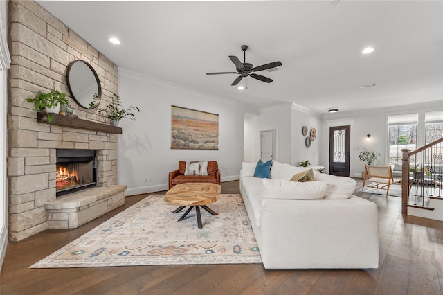 living room featuring stairs, ornamental molding, dark wood-type flooring, and a stone fireplace