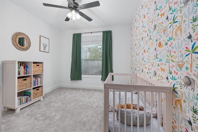 bedroom featuring carpet floors, a nursery area, baseboards, and a ceiling fan