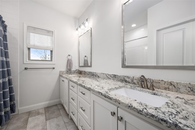 full bathroom with double vanity, tile patterned flooring, a sink, and baseboards