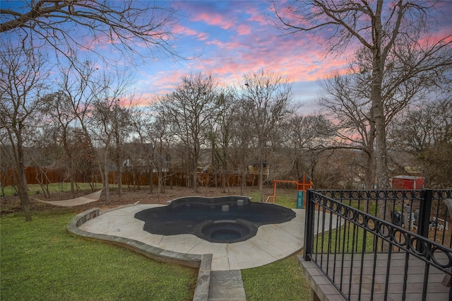 pool at dusk featuring an outdoor hot tub, fence, and a yard