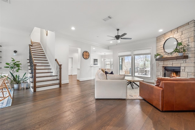 living area featuring dark wood-type flooring, a fireplace, visible vents, a ceiling fan, and stairway