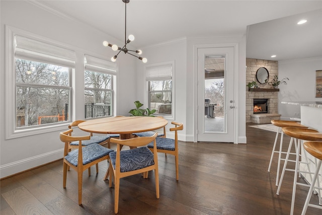 dining space featuring dark wood-style floors, baseboards, crown molding, and a stone fireplace