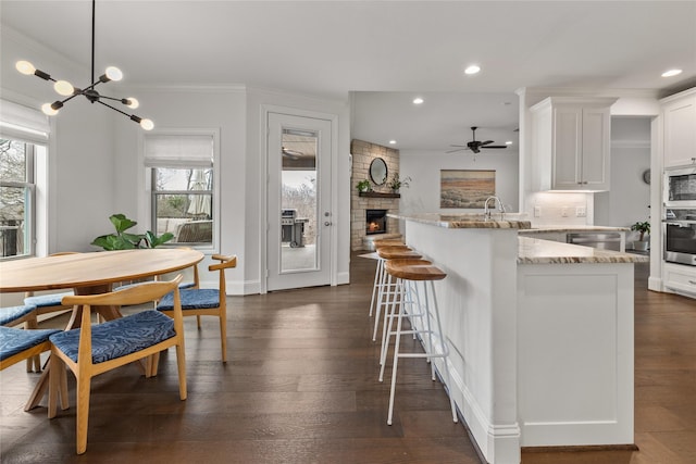 kitchen with light stone counters, stainless steel appliances, white cabinets, a stone fireplace, and a peninsula