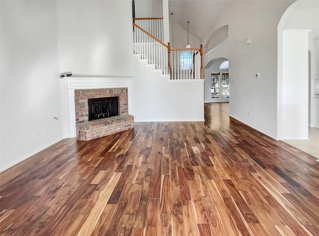 unfurnished living room featuring a brick fireplace, wood-type flooring, and a high ceiling