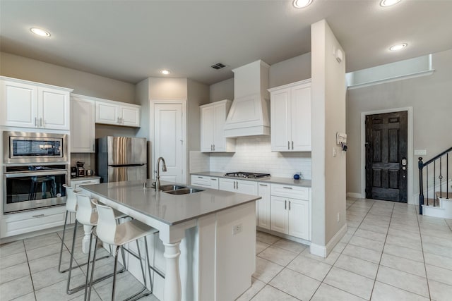 kitchen with a center island with sink, sink, custom exhaust hood, stainless steel appliances, and white cabinets