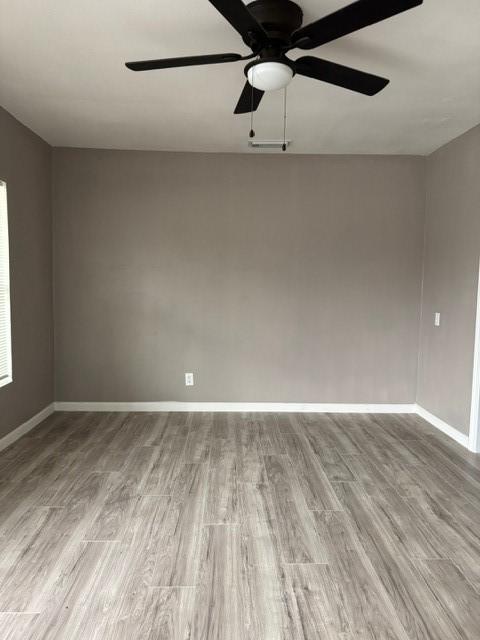 empty room featuring a ceiling fan, wood finished floors, visible vents, and baseboards