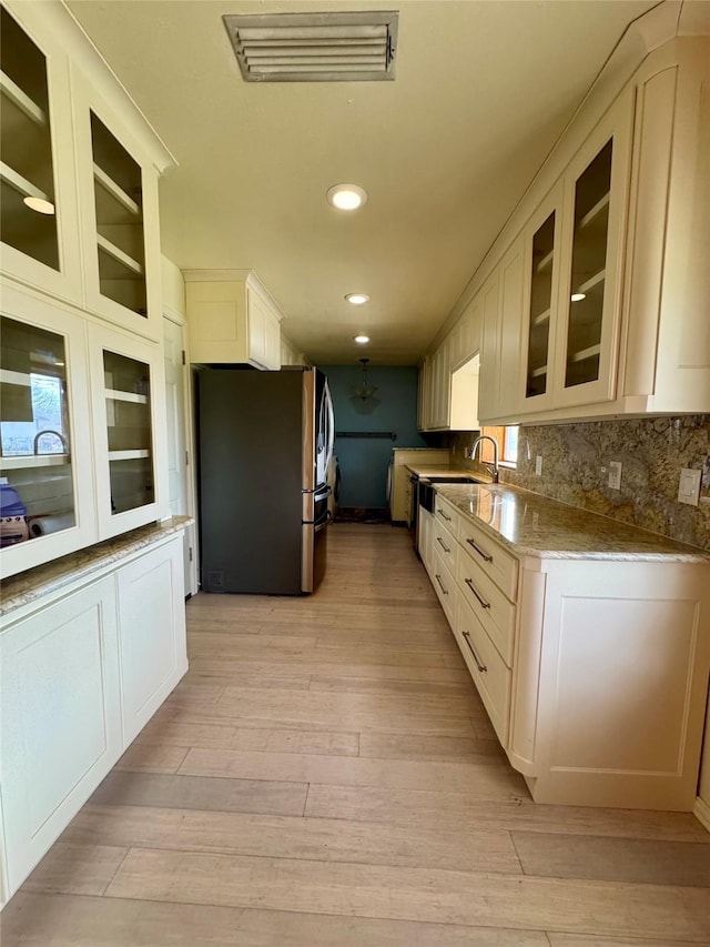 kitchen with light hardwood / wood-style flooring, light stone countertops, stainless steel fridge, sink, and white cabinetry