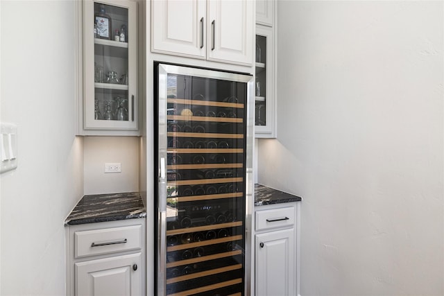 bar with white cabinets, dark stone countertops, and beverage cooler