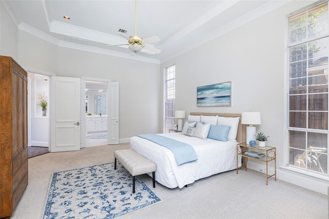 carpeted bedroom with ceiling fan, ornamental molding, a raised ceiling, and ensuite bath