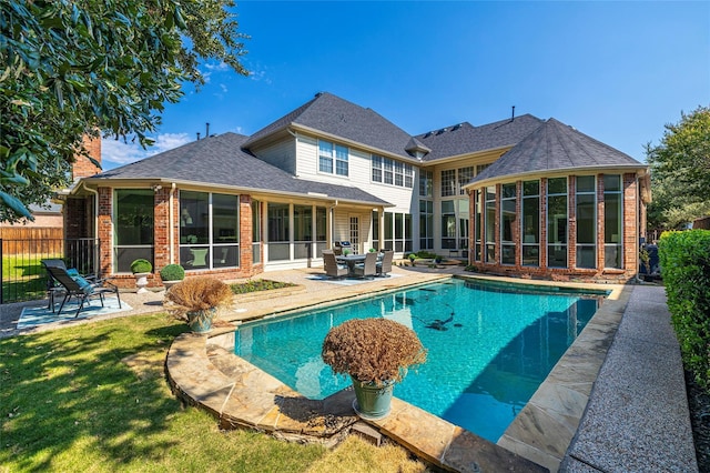 back of property with a sunroom, a lawn, a fenced in pool, and a patio area