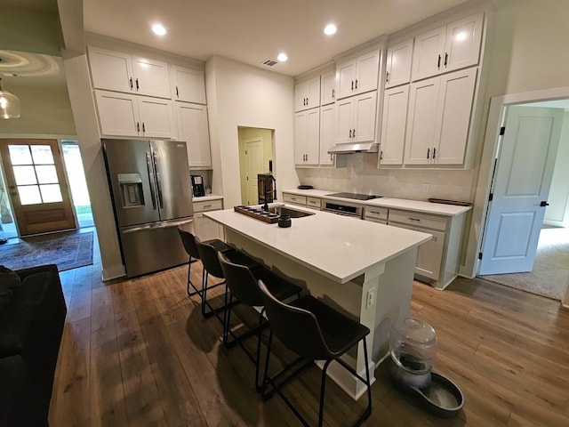 kitchen with a breakfast bar area, a kitchen island with sink, stainless steel appliances, white cabinetry, and light countertops