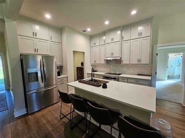 kitchen featuring a kitchen island with sink, a breakfast bar, a sink, light countertops, and stainless steel fridge