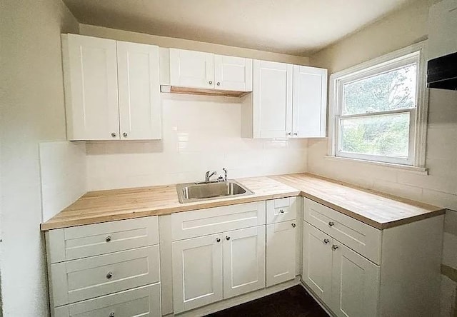 kitchen featuring wooden counters, white cabinetry, and sink